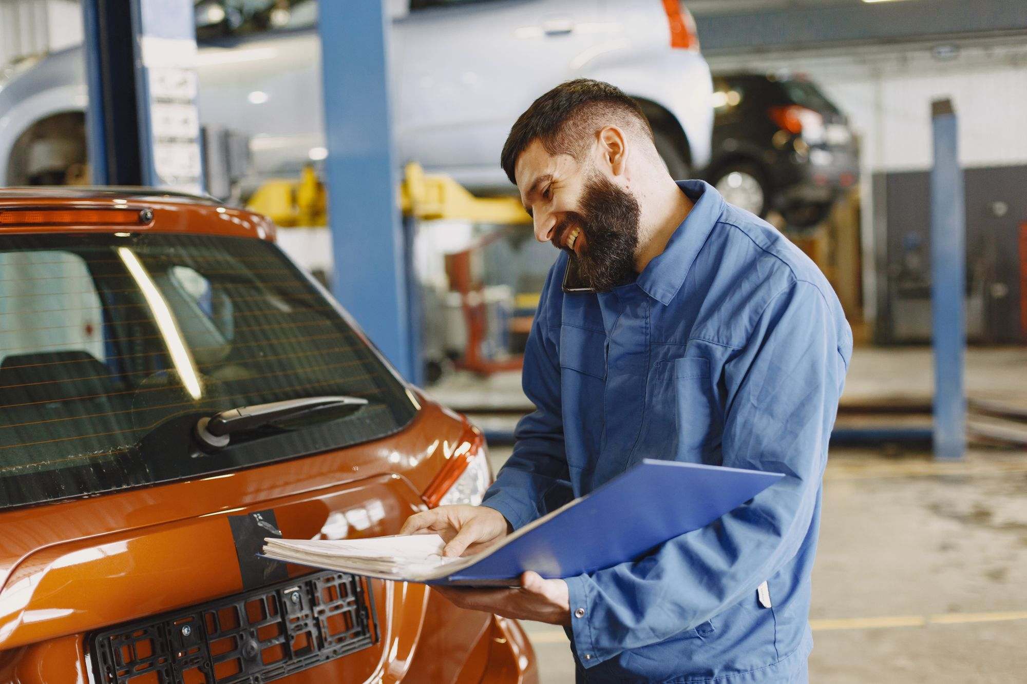 A mechanic with a clipboard beside a car in a repair shop