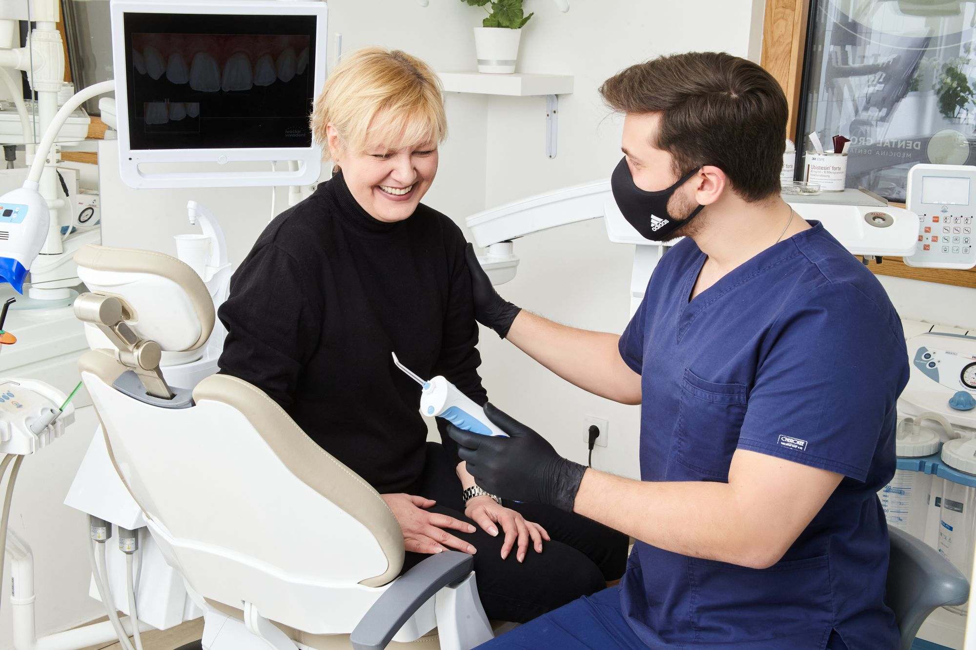 A dentist talking with a smiling patient in a treatment room