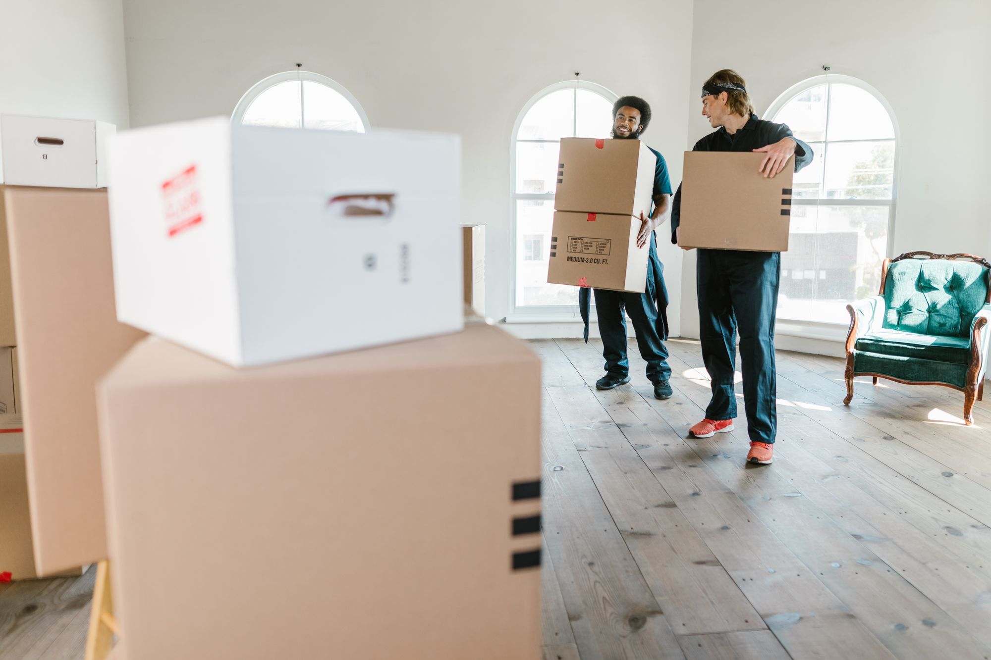 Two movers carrying boxes through a bright room