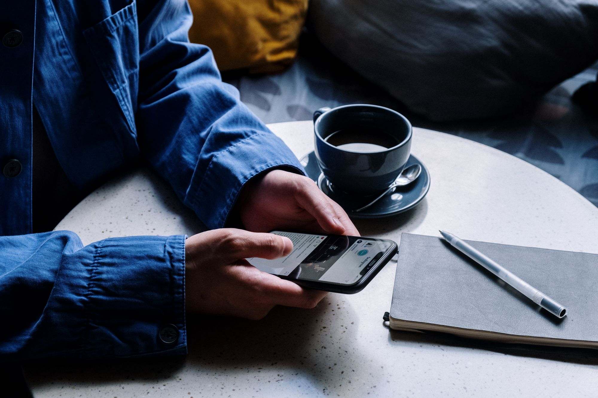A person checking a smartphone next to a coffee and notepad