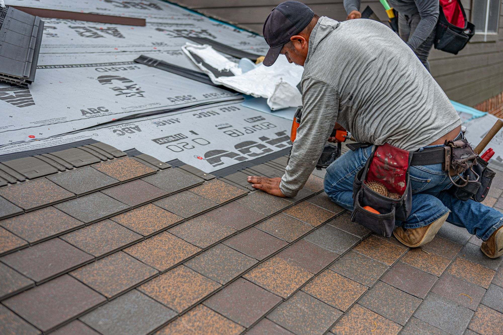 A roofer laying new asphalt shingles on a house roof