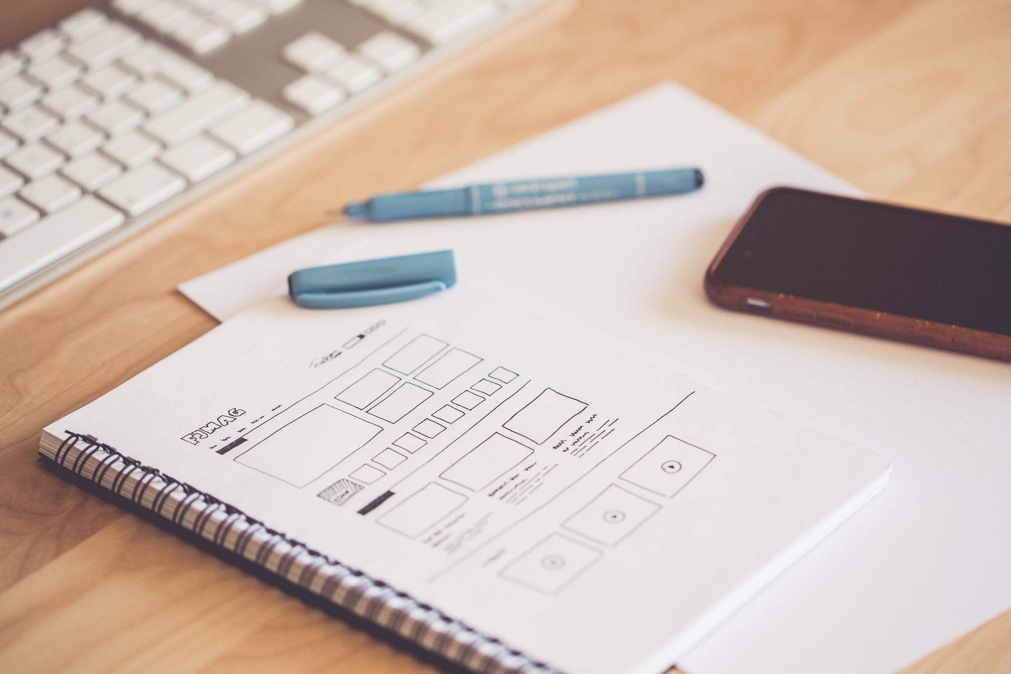 Website wireframe sketches beside a phone and keyboard