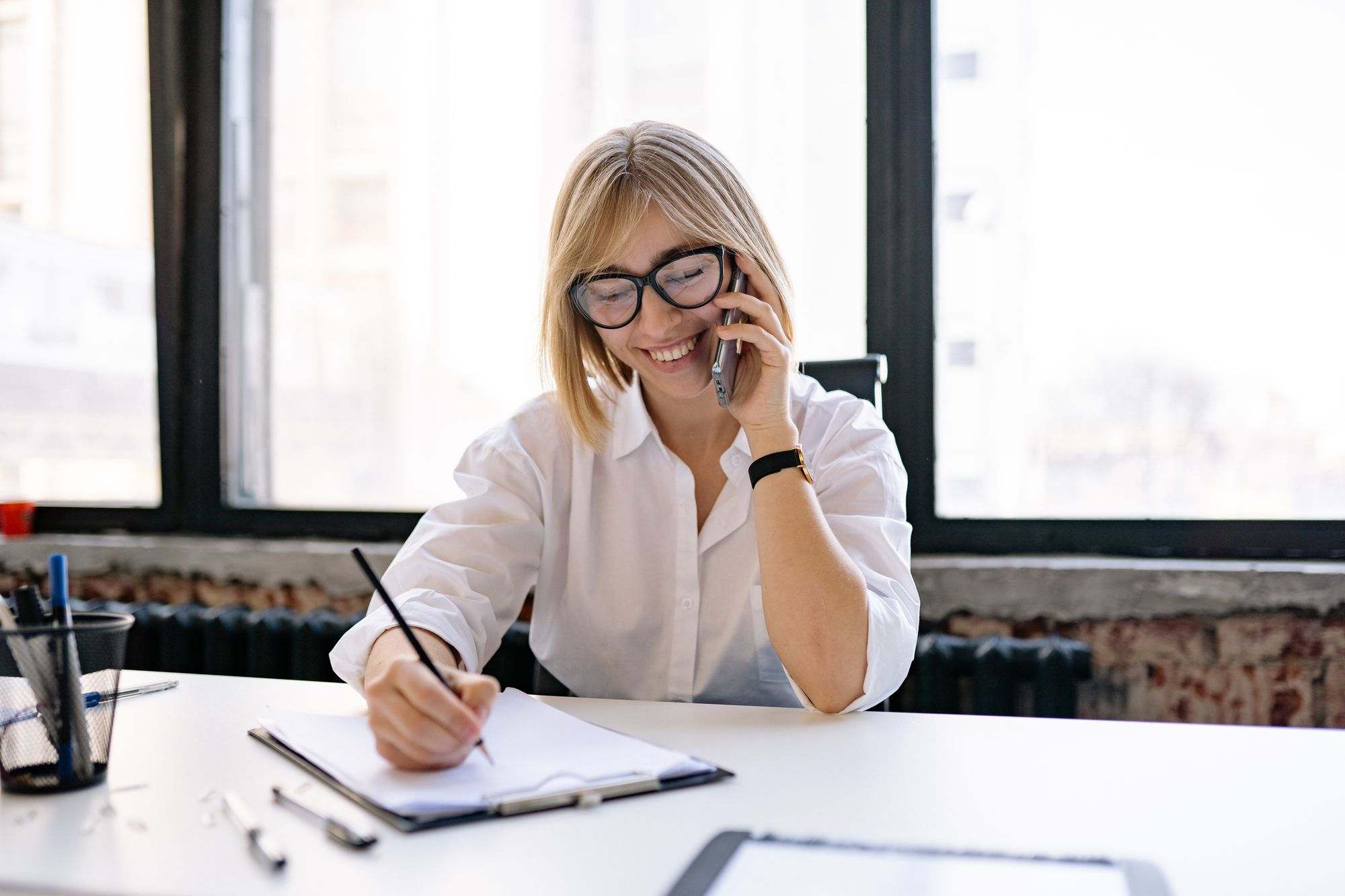 A woman taking notes during a phone call at her desk